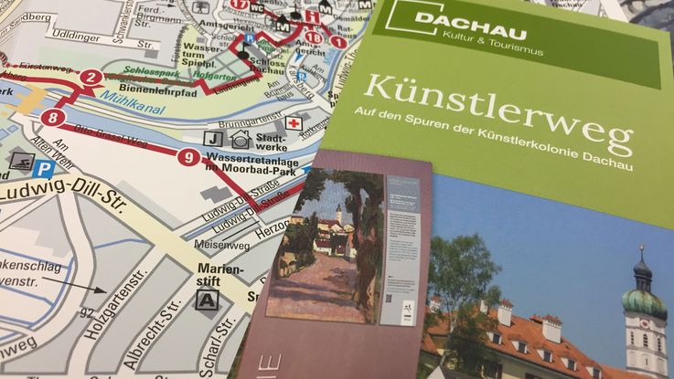 Das Foto zeigt einen Flyer des Künstlerwegs Dachau, der auf einem aufgeklappten Flyer zum Künstlerweg liegt. Hier ist die Karte von Dachau sichtbar.