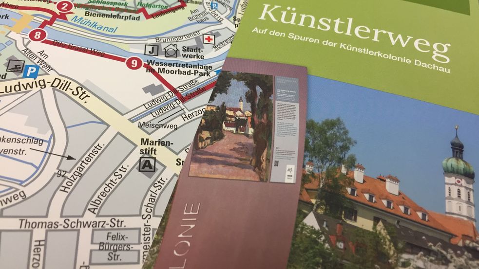 Das Foto zeigt einen Flyer des Künstlerwegs Dachau, der auf einem aufgeklappten Flyer zum Künstlerweg liegt. Hier ist die Karte von Dachau sichtbar.