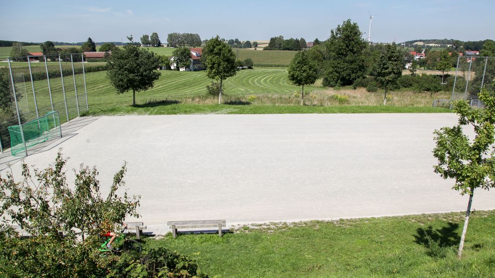 Befestigter Bolzplatz umgeben von Wiesen und Bäumen