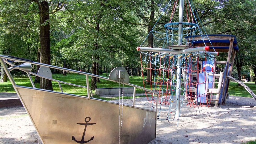 Spielschiff im Sand mit Schiffmastkletterturm umgeben von Bäumen