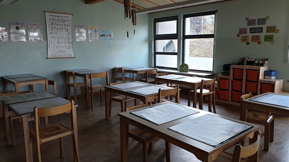 Lernraum mit großen, weißen Blättern auf den Tischen und Buchstabenalphabet an der Wand