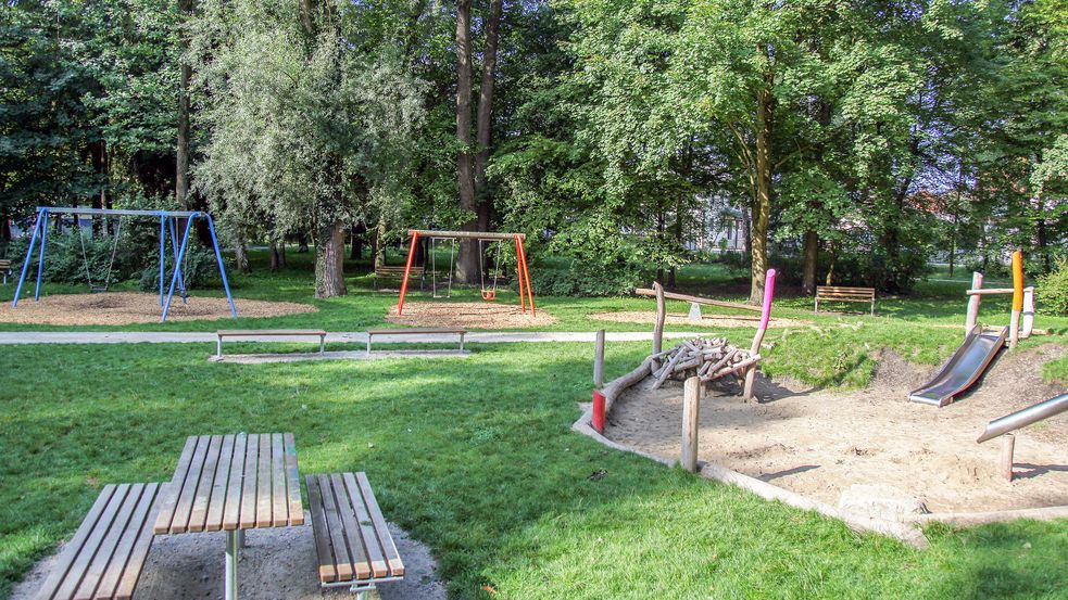 Tisch mit Bänken umgeben von Wiese mit Schaukeln und Sandkasten im Hintergrund