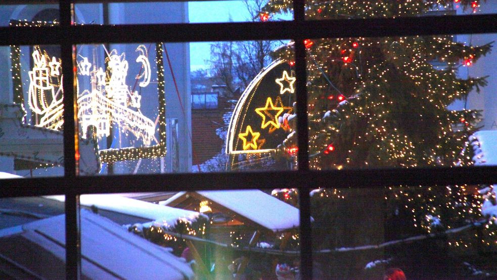 Blick durch Fenster auf den Christkindlmarkt mit Beleuchtung und Ständen