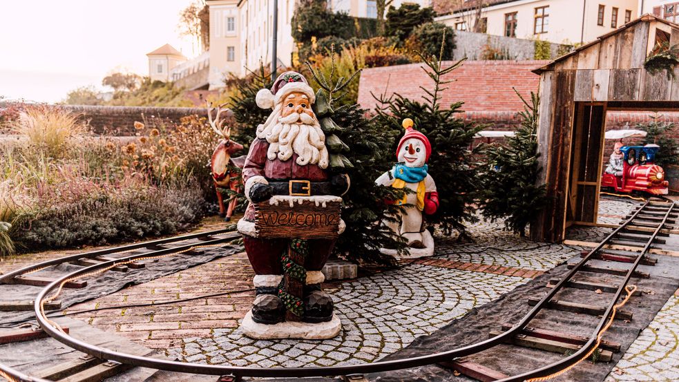 Nikolausholzfigur mit Schild Willkommen inmitten der Schienen der Kinderbimmelbahn