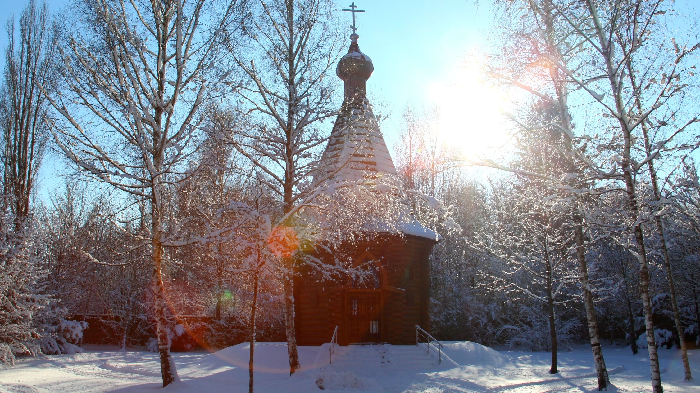 Fotografie der Christi-Auferstehungs-Gedächtniskapelle auf dem Gelände der KZ-Gedenkstätte in Dachau. Um die Kapelle liegt Schnee und die Sonne scheint durch die kahlen Bäume.