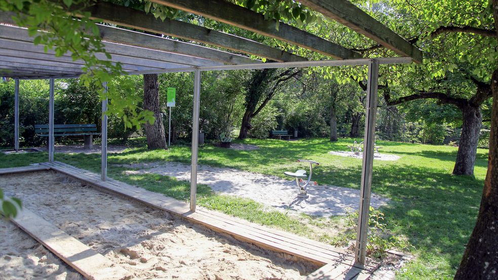 Pergola über Sandkasten neben Wiese mit Bäumen