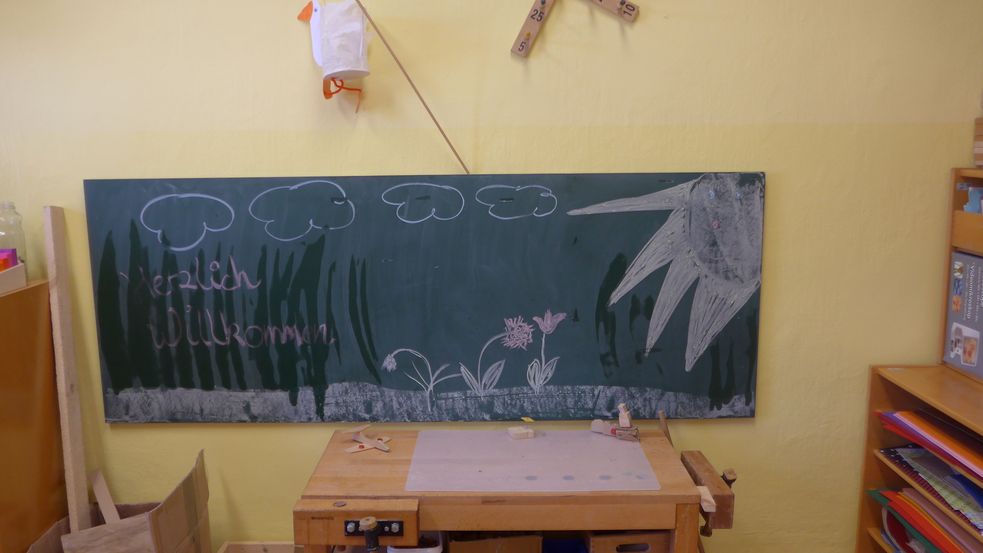 Schwarze Kreidetafel mit Willkommensgruß, Blumen und Sonne bemalt 