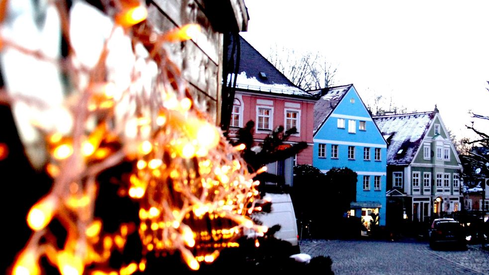 Weihnachtsbeleuchtung an Verkaufsstand, dahinter bunte Altstadthäuserfassaden