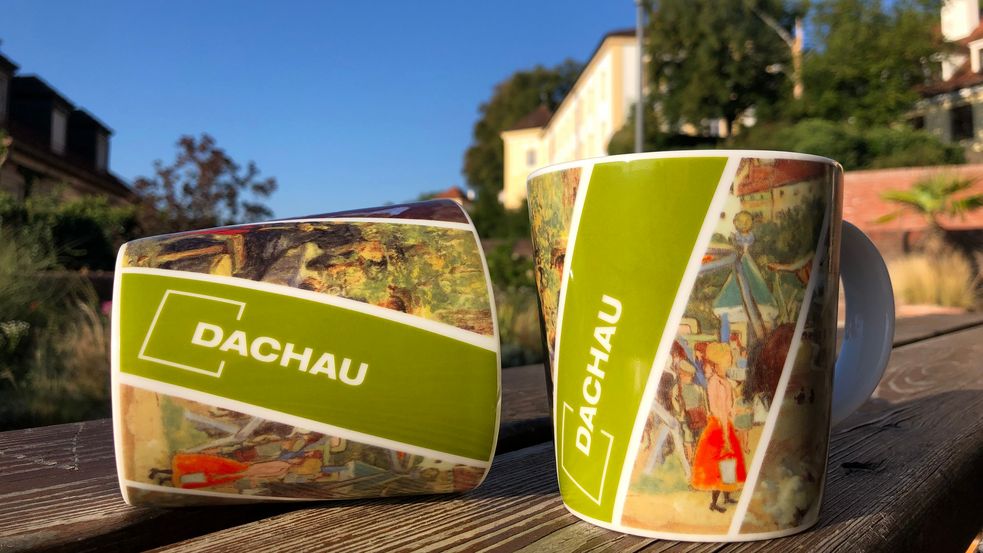 Souvenir der Stadt Dachau, eine Tasse mit schräg verlaufenden Streifen in denen alte Gemälde zu sehen sind. 1 Streifen ist mit dem Logo der Stadt Dachau.