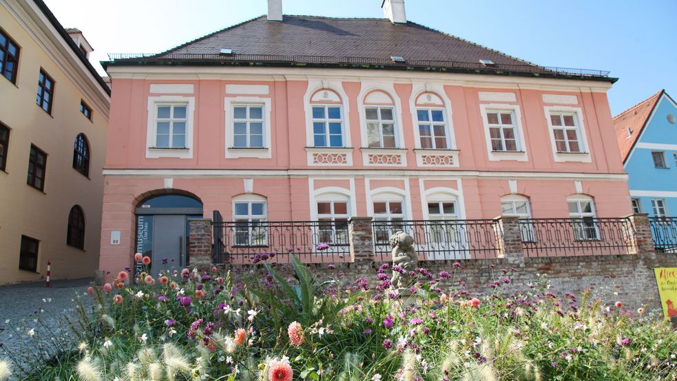 Photo of Dachau District Museum from the front with flower bed in front and blue sky above. Photo: City of Dachau