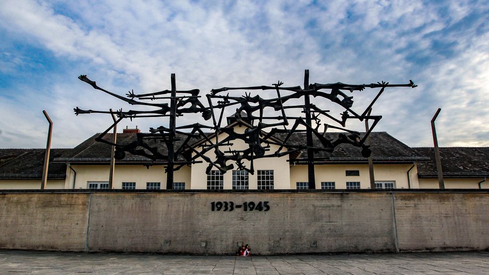 Phot of International Memorial in front of the "Jourhaus" at Concentration Camp Memorial Site Dachau. Dramatic blue sky with white streaming clouds. Photo: City of Dachau