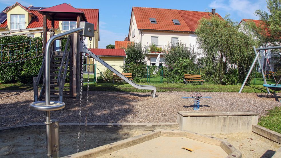 Sandkasten mit Rutsche, Schaukeln und Bank im Hintergrund