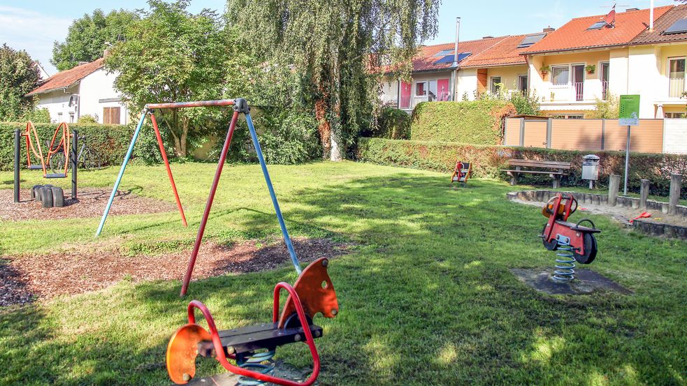 Wipptiere und Schaukeln auf Wiese mit Bänken und Wohnhäusern im Hintergrund