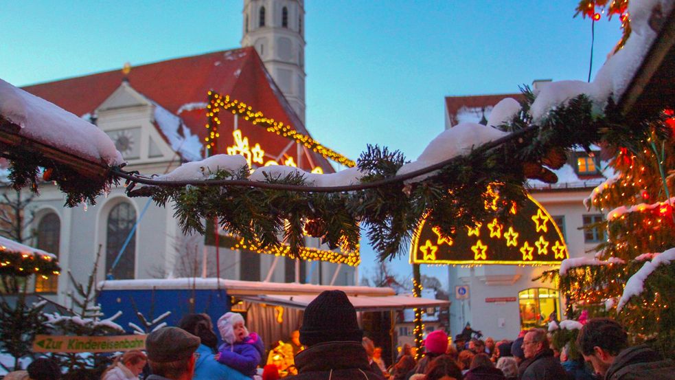Verschneiter Christkindlmarktstand und viele Besucher im Hintergrund