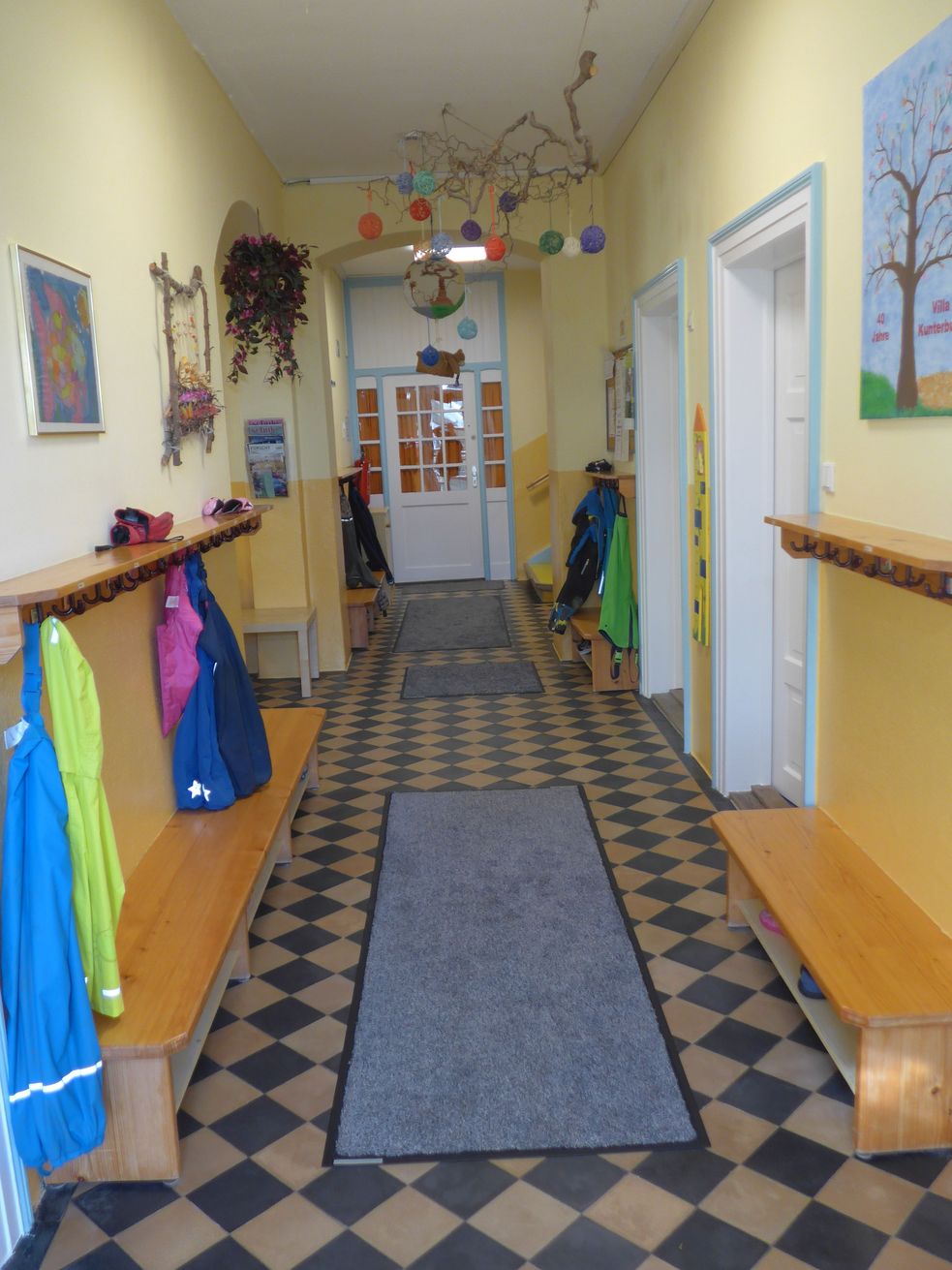 Eingangsbereich mit Bildern und Deko an den Wänden, seitlich eine Kinder-Garderobe mit Jacken