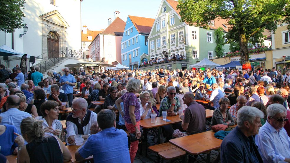 Viele Menschen sitzen an Tischen in einer Altstadtstraße