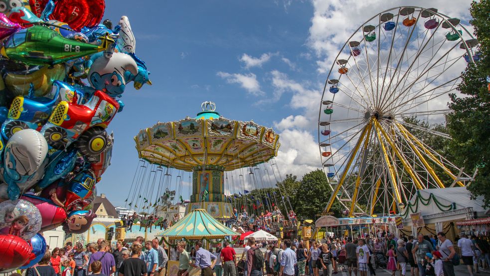 Besucher auf Volksfest mit Karussell und Riesenrad im Hintergrund