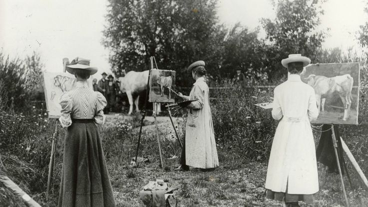 Black and white photographie of a womens' outdoor painting class around the year 1900 with easels and cow, trees in the background. Photo: Zweckverband Dachauer Galerien und Museen.