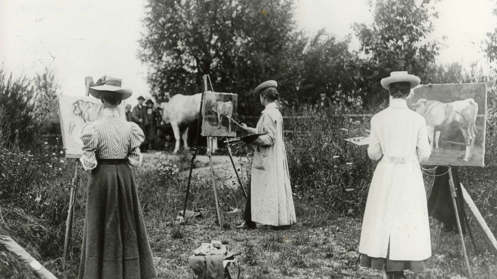 Black and white photographie of a womens' outdoor painting class around the year 1900 with easels and cow, trees in the background. Photo: Zweckverband Dachauer Galerien und Museen.