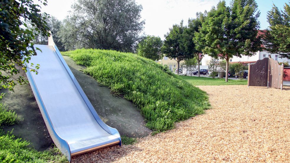 Eine Rutsche im Hintergrund eine Kletterwand und Bäume