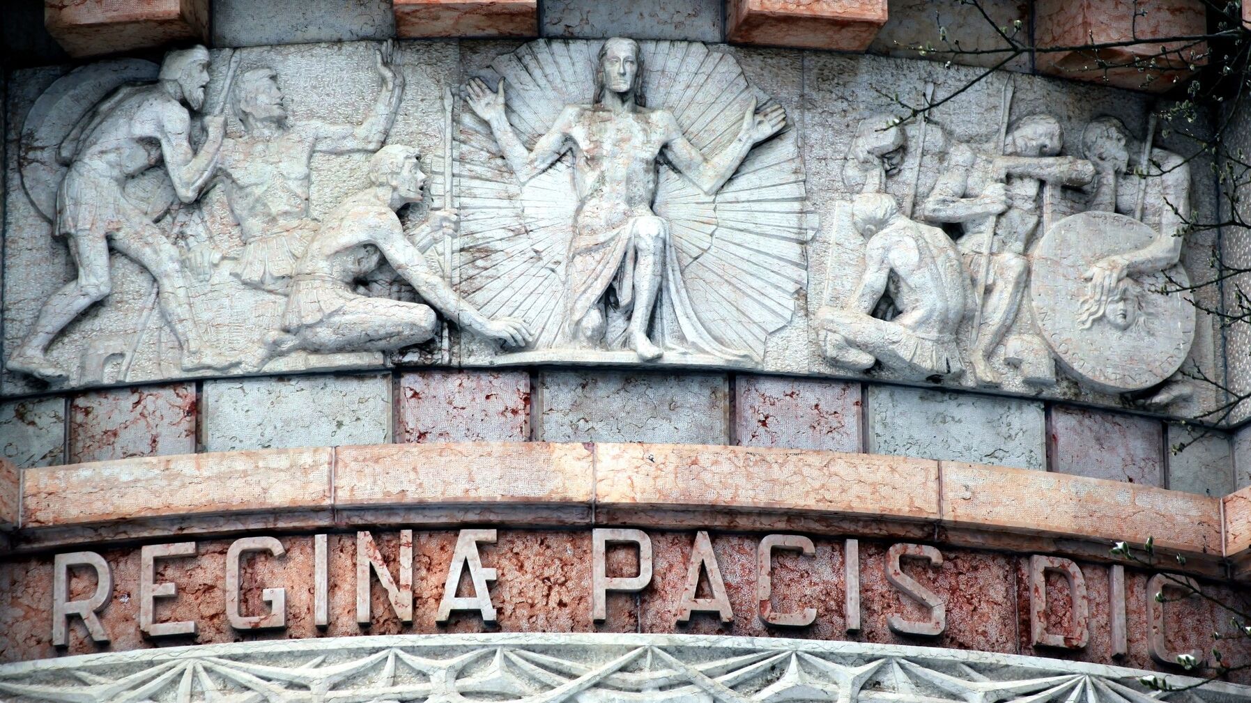 Detailfotografie eines Reliefs an der Kapelle "Regina Pacis" auf dem Dachauer Leitenberg. Das Relief zeigt Jesus umstrahlt und von flehenden Menschen umgeben.