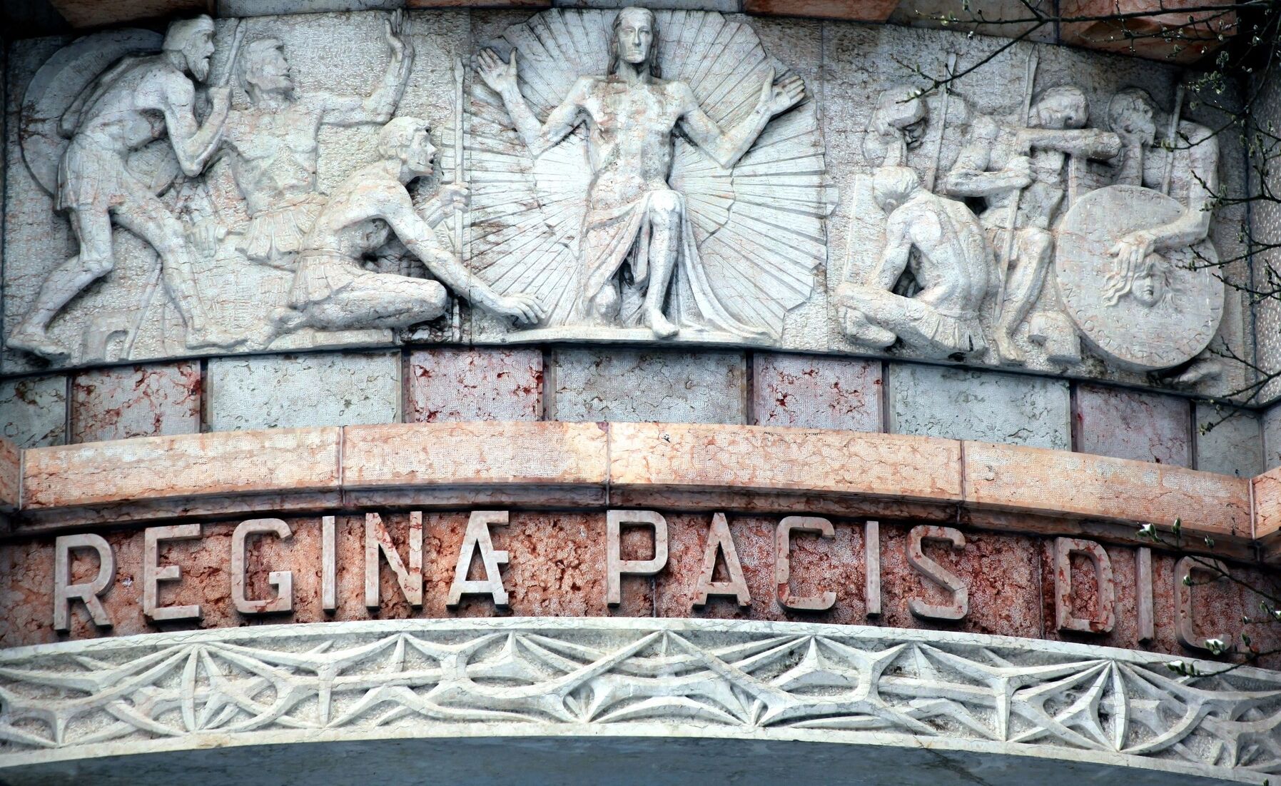 [Translate to English:] Detailfotografie eines Reliefs an der Kapelle "Regina Pacis" auf dem Dachauer Leitenberg. Das Relief zeigt Jesus umstrahlt und von flehenden Menschen umgeben.
