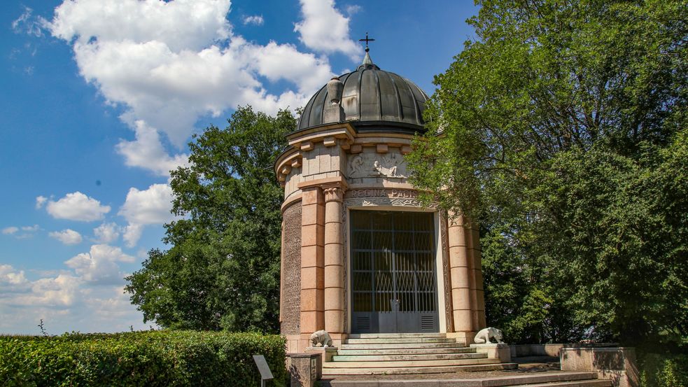 Photo of Italian memorial chapel "Regina Pacis" in summer with green trees and blue sky. Photo: City of Dachau