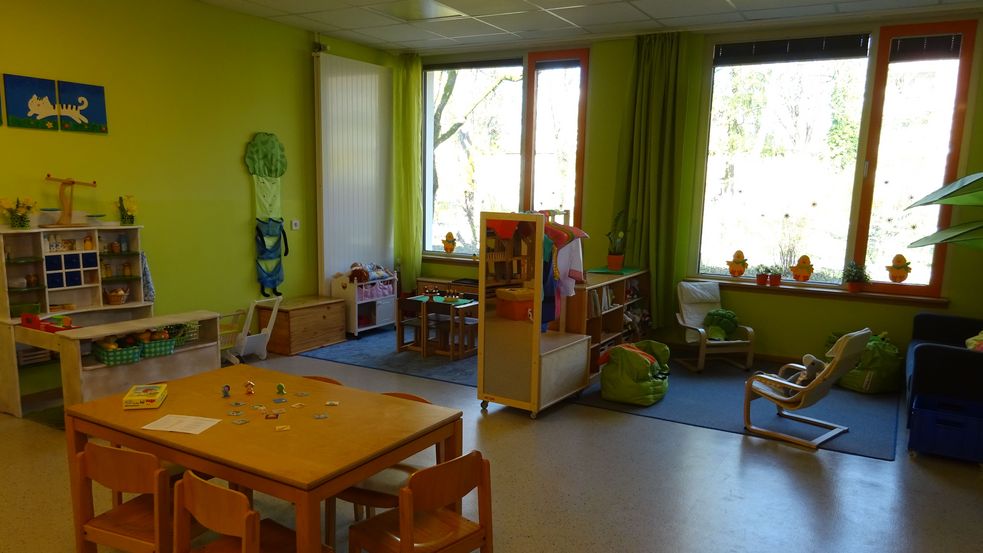 Aufenthaltsraum in grün mit Tischen, Stühlen, Regalen und Spielsachen mit Spielecke 