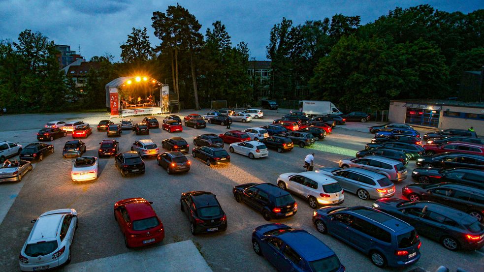Vielen Autos stehen auf einem großen Platz vor einer Bühne geparkt