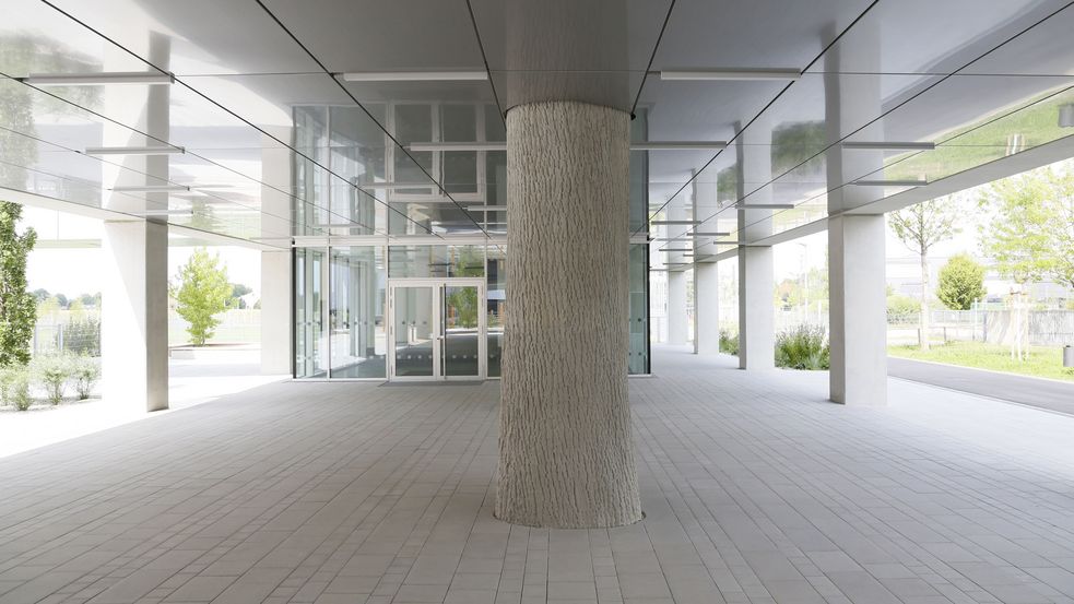 Modernes Gebäude, nach beiden Seiten hin offen, in der Mitte eine Säule, die einem Baum ähnelt.