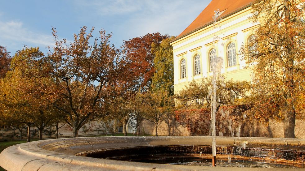 Steinerner Springbrunnen umgeben von Bäumen mit herbstlich gefärbten Blättern