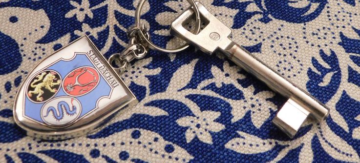 Photo of a room key with key-ring showing the coat of arms of the City of Dachau on blue and white tablecloth. Photo: P. Töpperwien