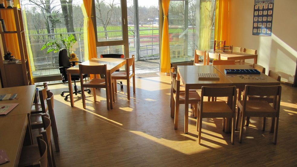 Sonnendurchfluteter Raum mit mehreren Tischen und Blick ins Grüne durch Fensterfront