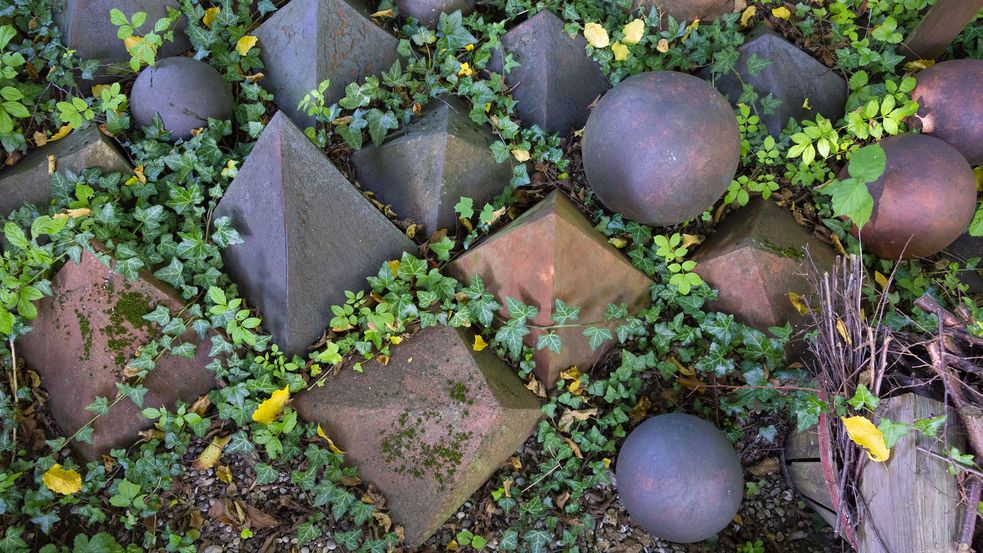 Kleine Skulpturen in Form von Pyramiden und Kugeln in Efeu