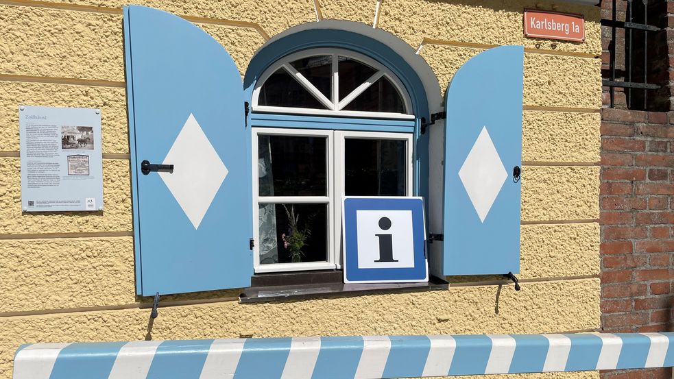 Fenster des historischen Zollhäusls, der neuen Dachauer Tourist-Information. Gekennzeichnet durch ein schwarzes I auf weißem Grund und blauem Rahmen.