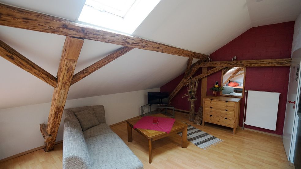 Foto der Innenräume der Ferienwohnung Lerchl, abgebildet wird hier die Sitzecke mit Couch und Fernseher in einer Dachschräge mit Holzbalken.