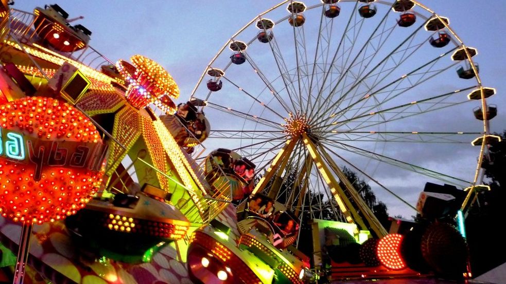 Coulorful illuminated rides at the traditional Dachau country fair, the Ferris wheel in the background, dusk is already setting in.