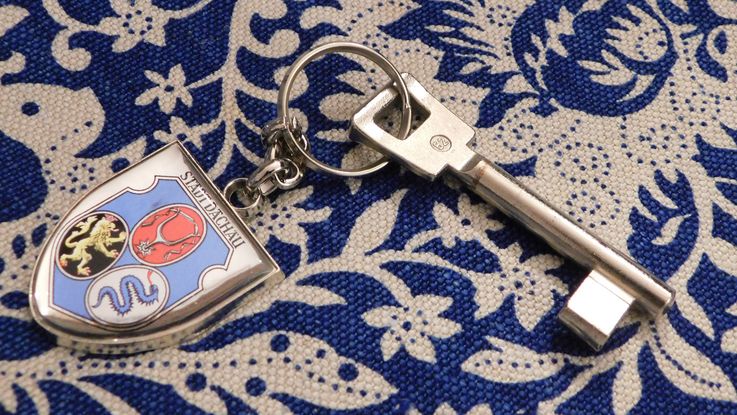 Photo of a room key with key-ring showing the coat of arms of the City of Dachau on blue and white tablecloth. Photo: P. Töpperwien