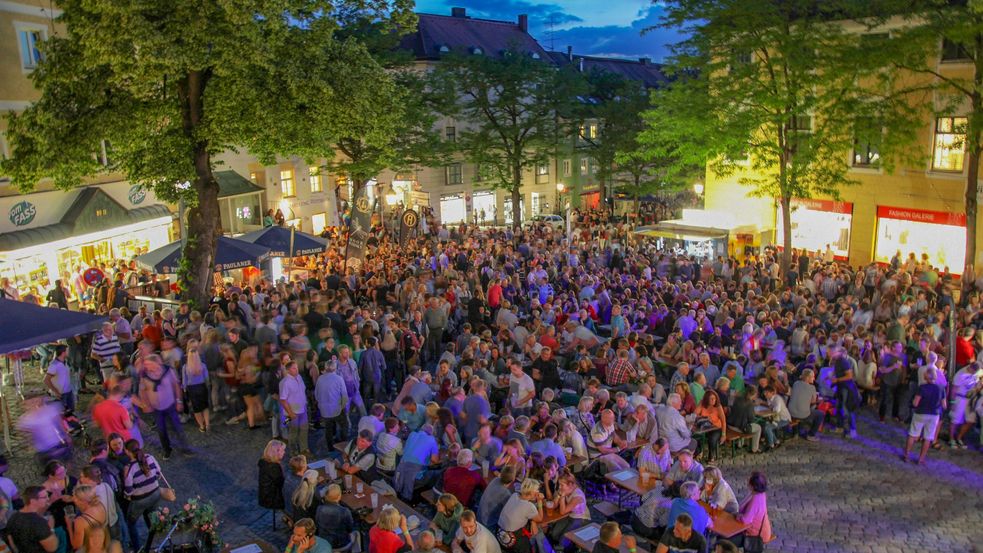 Viele Menschen sitzen an Tischen auf einem Dachauer Altstadtplatz