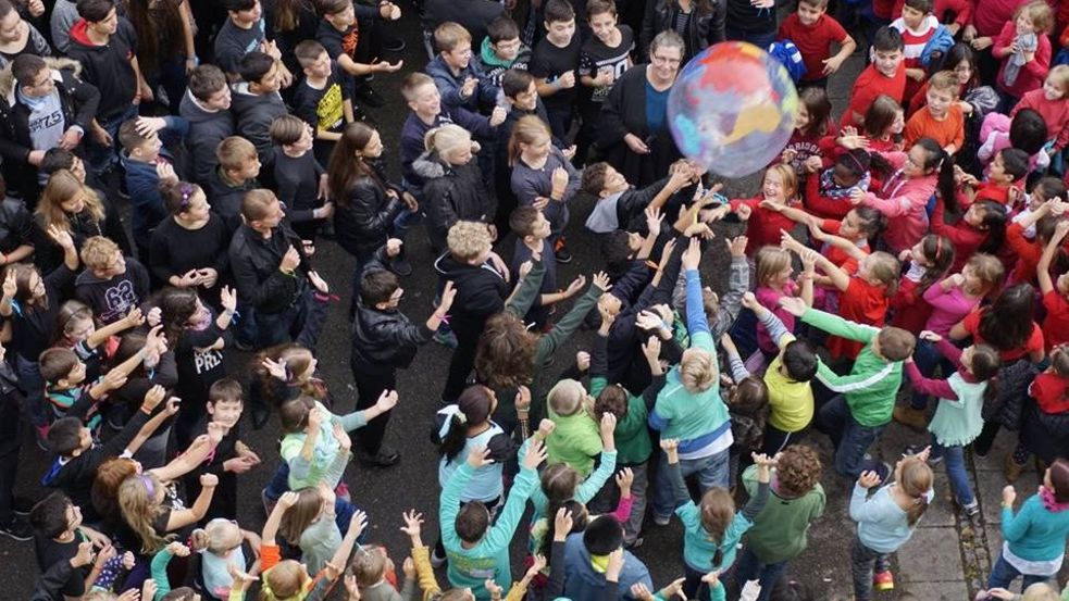 Bunt gekleidete Schülerinnen und Schüler spielen mit einer Weltkugel
