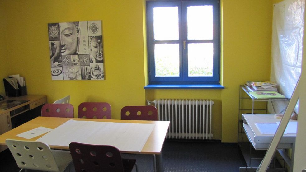 Raum mit gelben Wänden, Tisch mit Stühlen und Buddha-Bild an der Wand