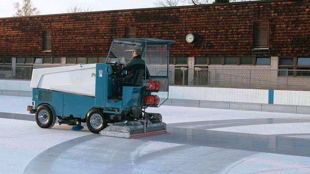 Mann fährt in einer Eisbearbeitungsmaschine über die Kunsteisbahn und hinterlässt nasse Streifen auf dem Eis