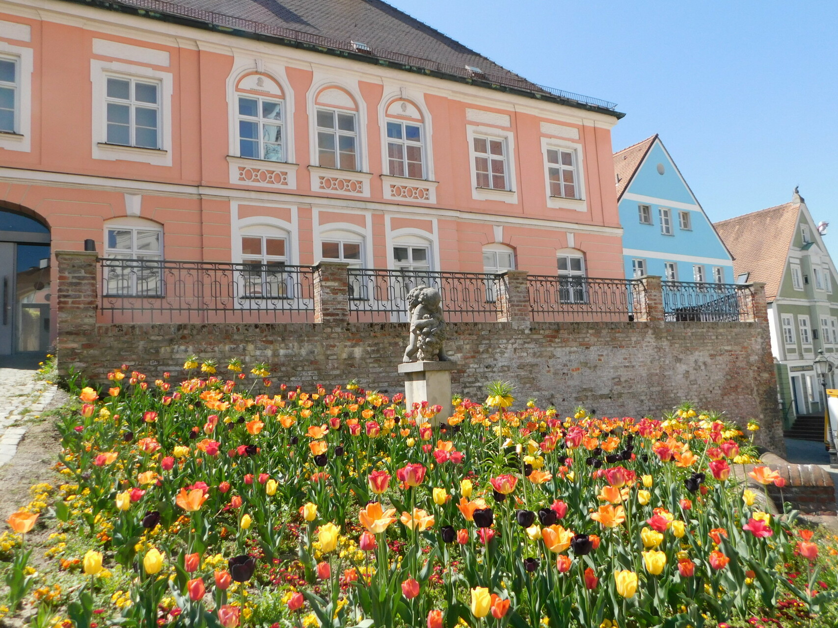 Außenansicht Bezirksmuseum Dachau mit Blumenbeeten und Putto-Statue im Vordergrund