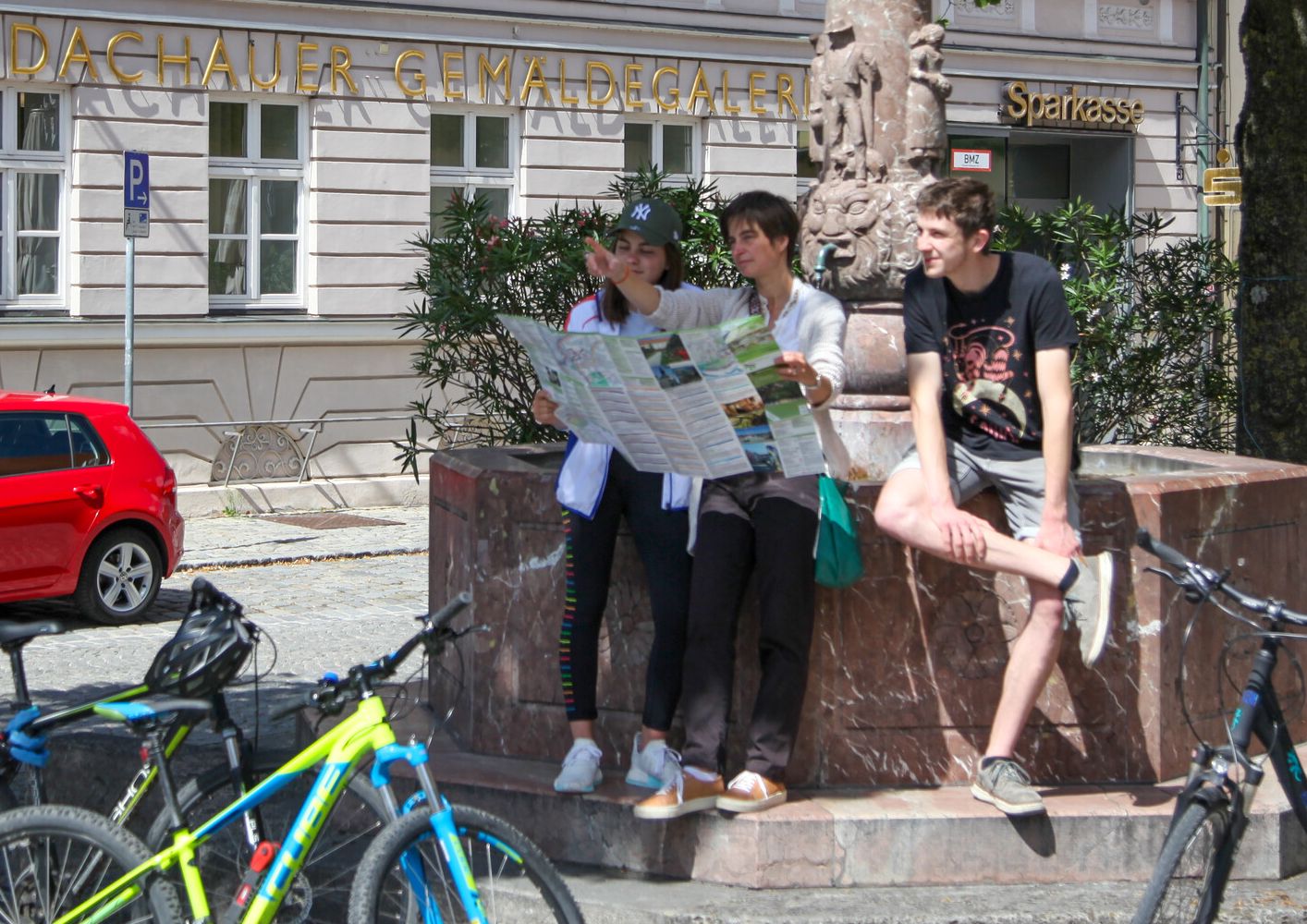 Radfahrer stehen am Taschne-Brunnen in Dachau und schauen in Radl-Karte